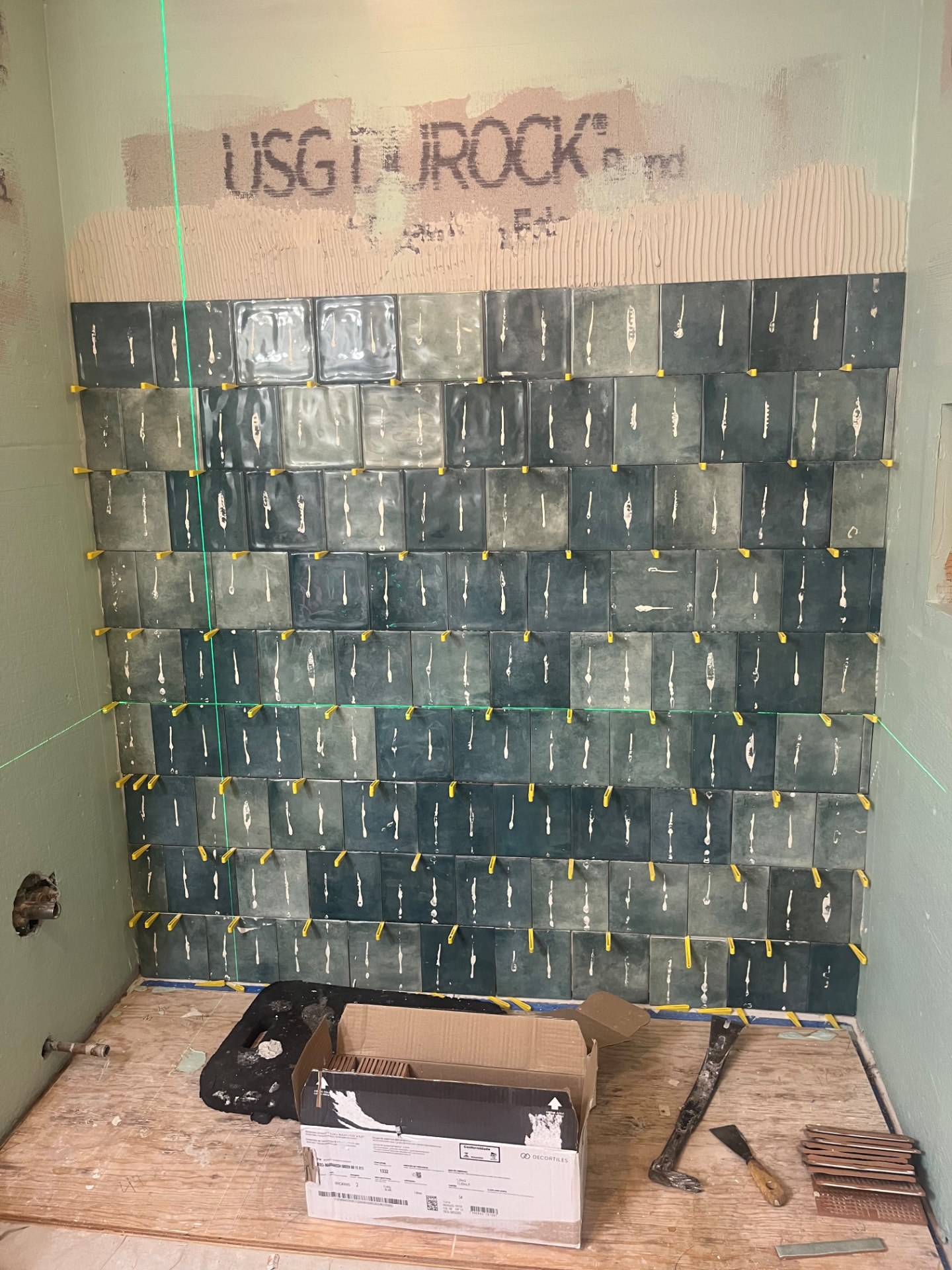 Green subway tile being set in a shower with a laser level and spacers