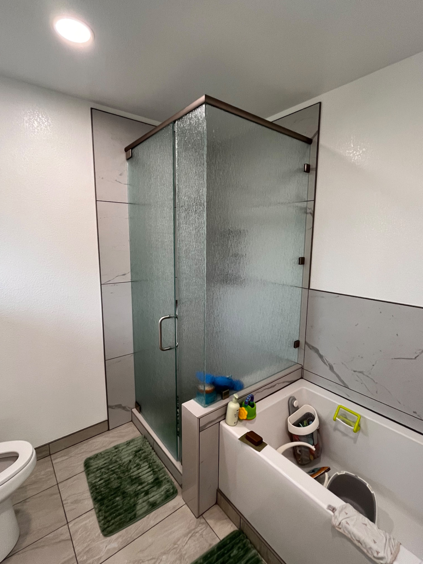 Finished bathroom remodel with a frameless glass shower enclosure, tiled tub surround and new tile flooring