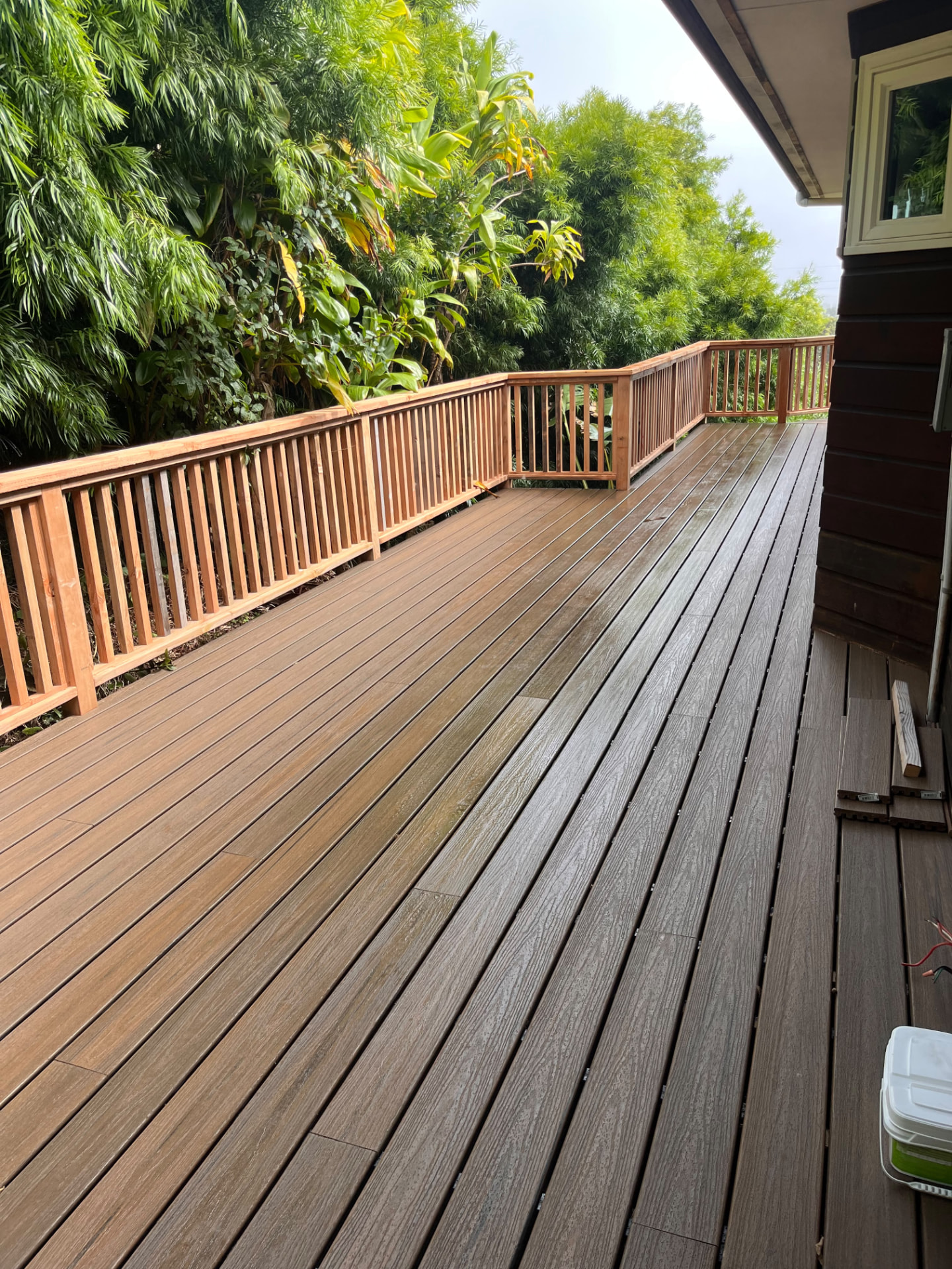 Finished composite deck with new wood railing along tropical greenery