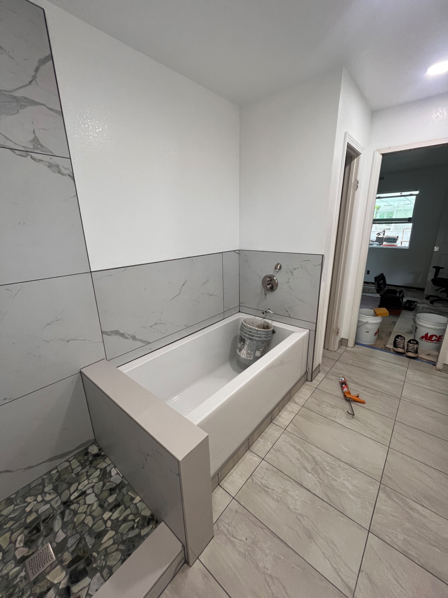 Tiled tub surround and pebble stone shower floor near completion