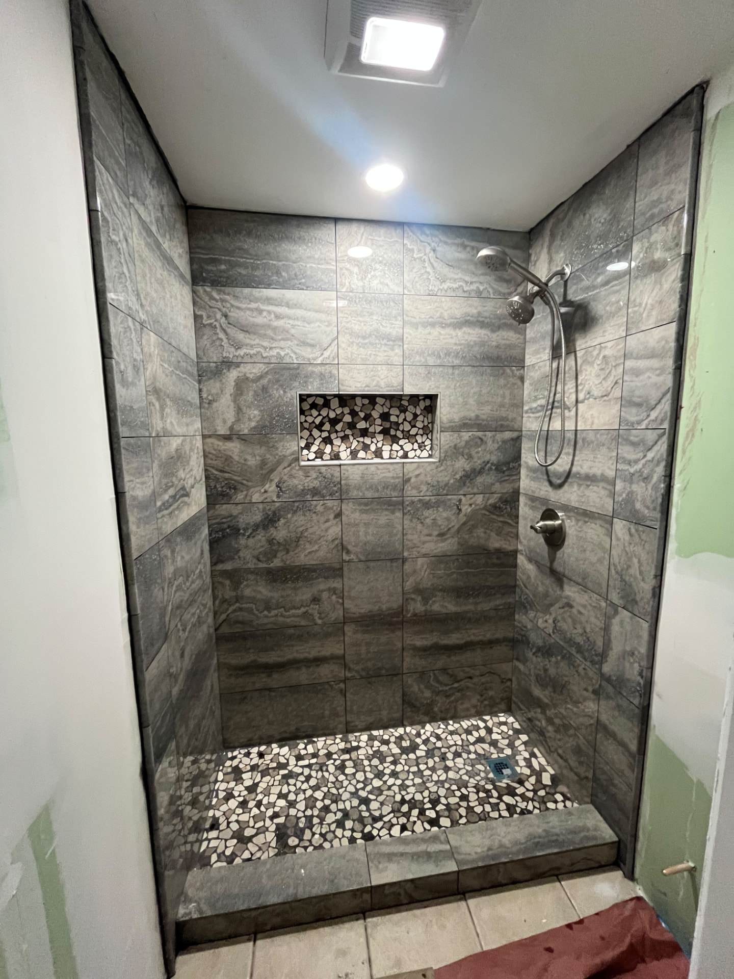 Finished gray tile shower with pebble floor and niche