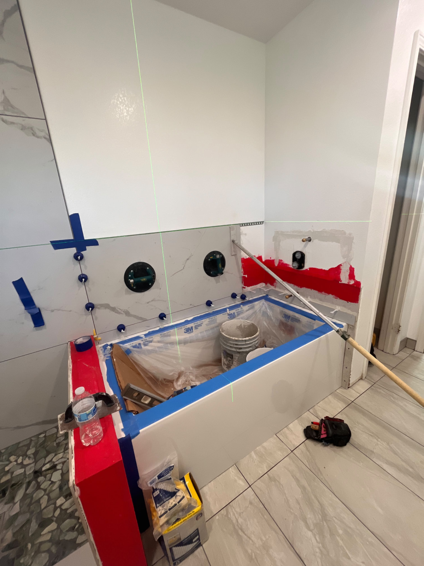 Large-format tile being set around a new bathtub with a laser level